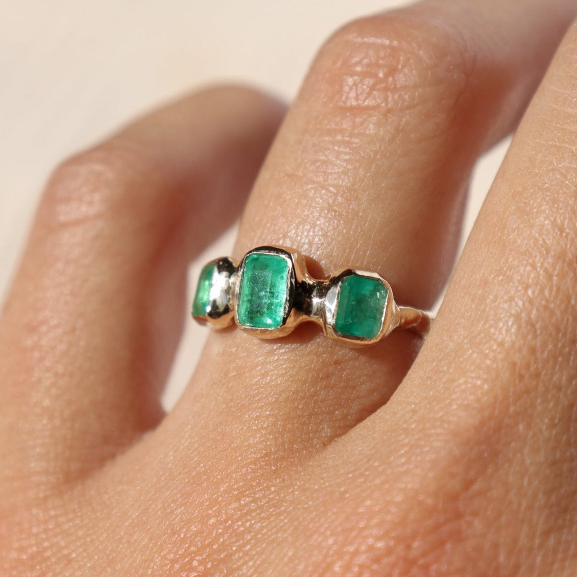 a trio emerald ring set in 14k gold worn on a ring finger