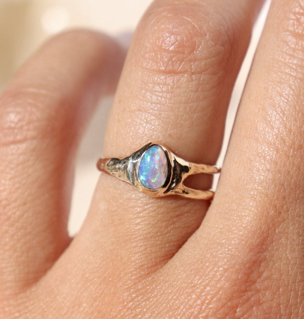 a small pear shaped opal set in 14k gold with an asymmetric band design is worn on a ring finger