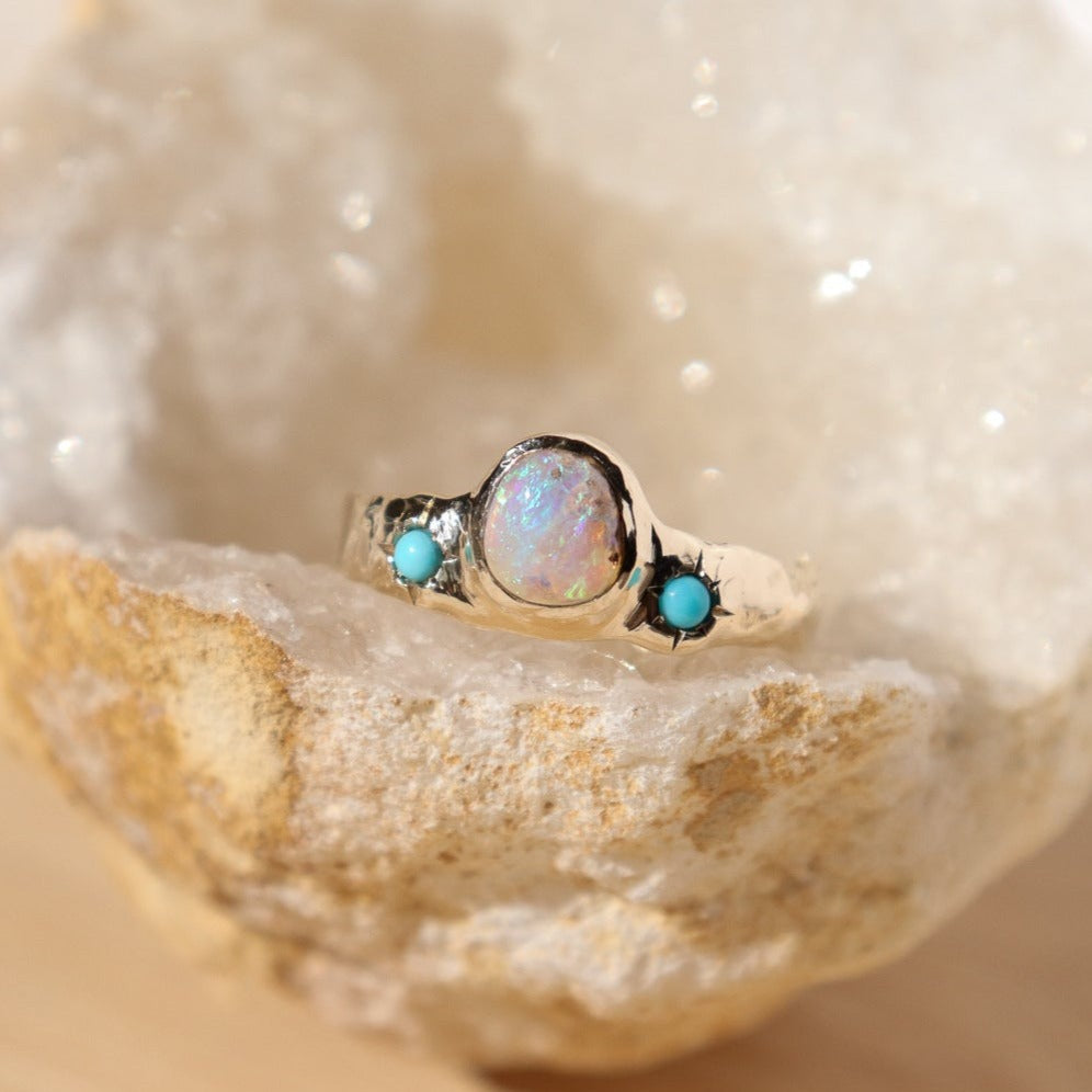 a wide gold band with a center opal and turquoise star settings is set on a crystal geode