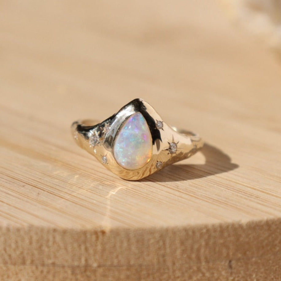 front view of a pear shaped opal gold ring with star set diamond accents