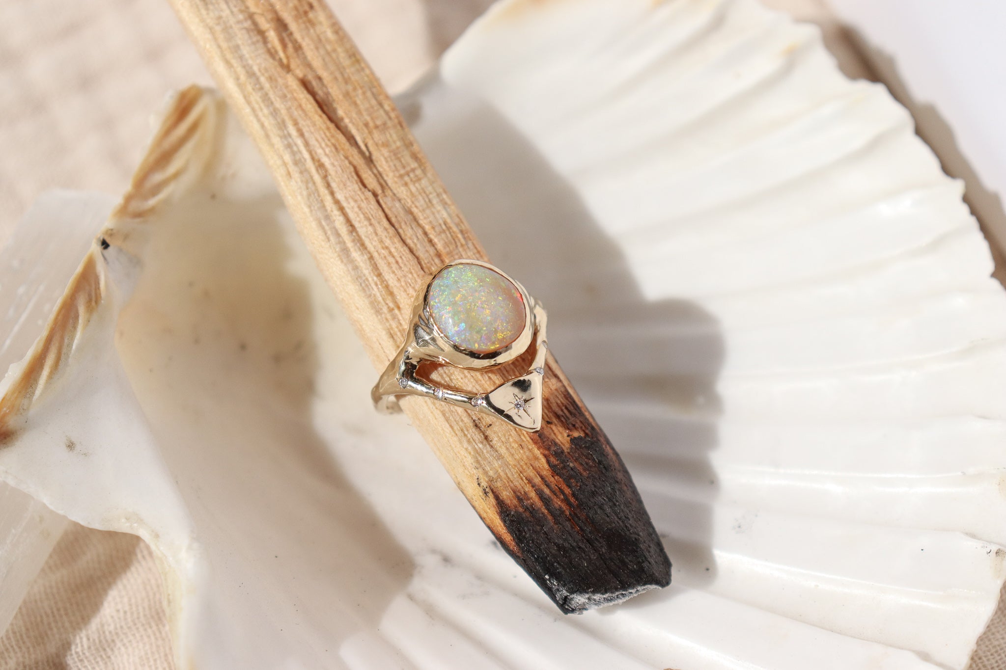 gold opal ring with diamonds is pictured on a palo santo stick and seashell dish