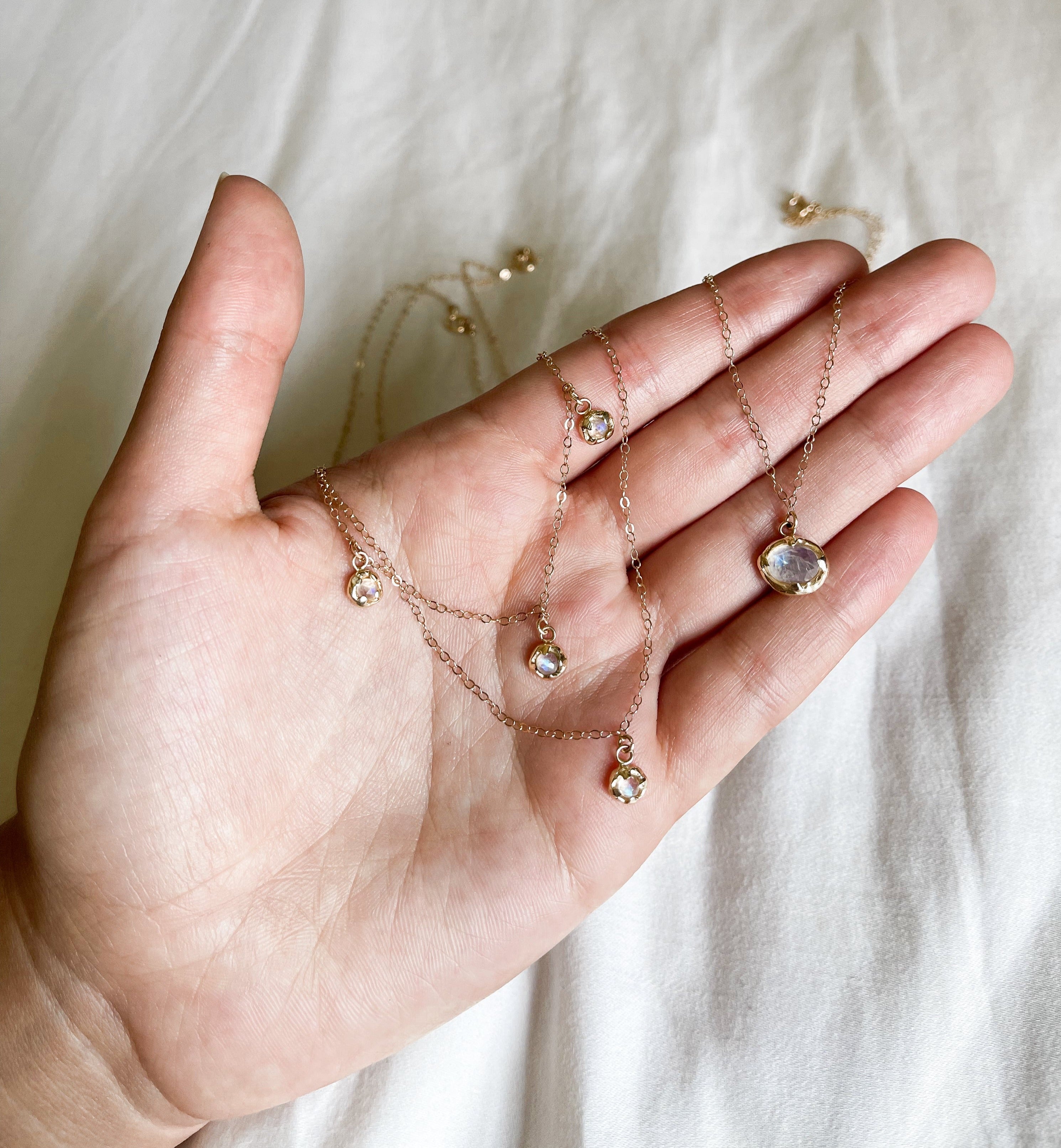 Dainty gold chains with moonstone charms are being held in an open hand