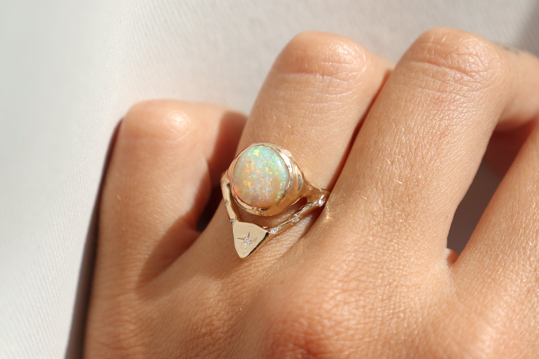 gold opal ring with diamonds is shown on a ring finger in direct sunlight, emphasizing the sparkles in the opal