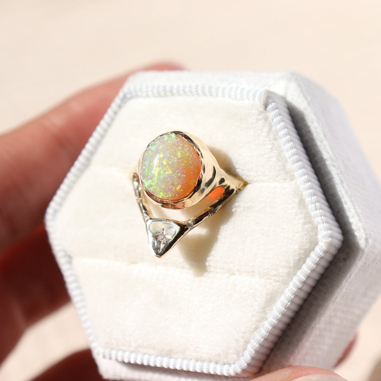 a gold opal ring with diamonds is in a white velvet ring box