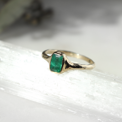 An emerald cut emerald is bezel set in 14k gold.