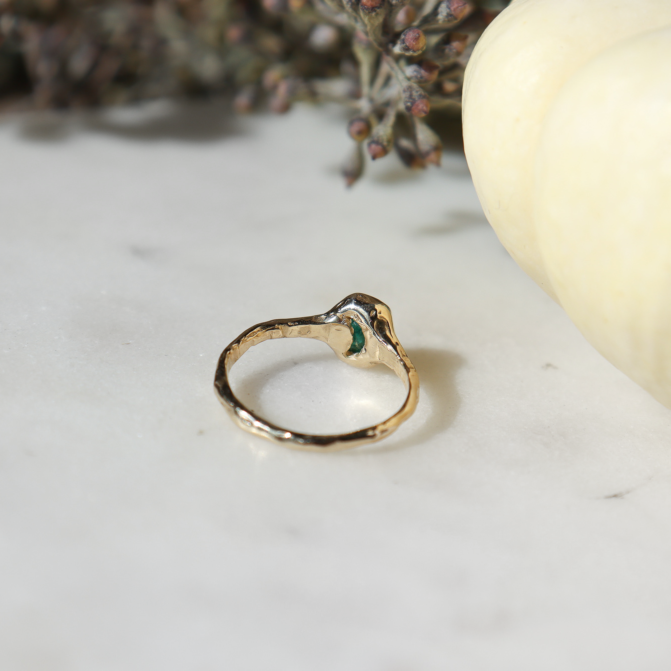 Back view of an emerald cut emerald that is bezel set in 14k gold with a small moon cut out  of the back.