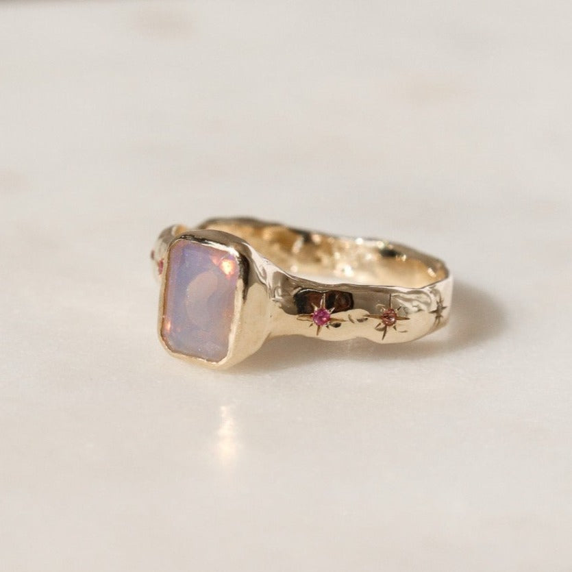An emerald cut opal is bezel  set  in 14k  gold  with a wide  band that  features  ombre sapphires  star  set a long  each side of the band.