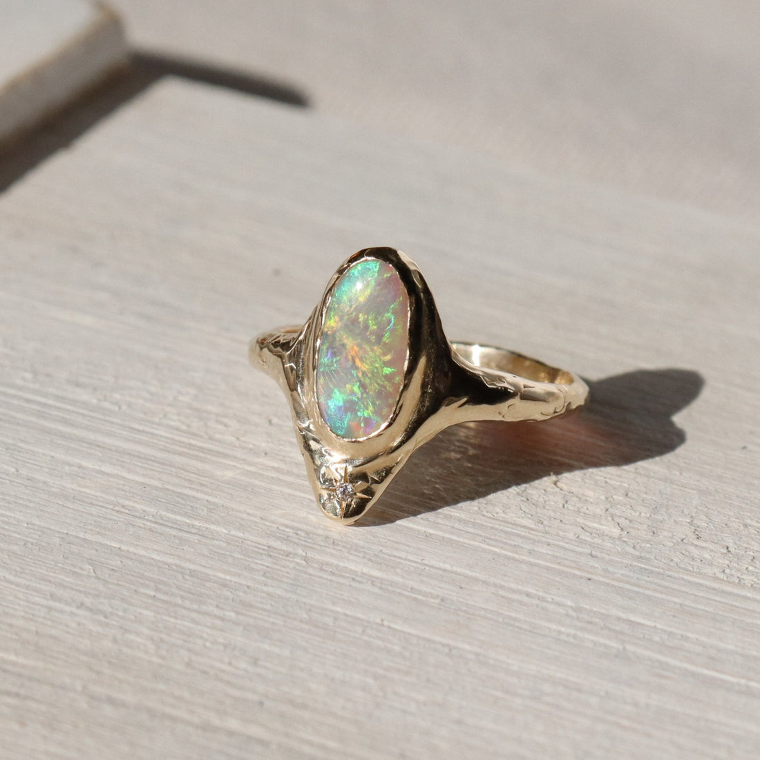 A long oval opal is bezel set in 14k gold with a star set diamond at the base of the ring.