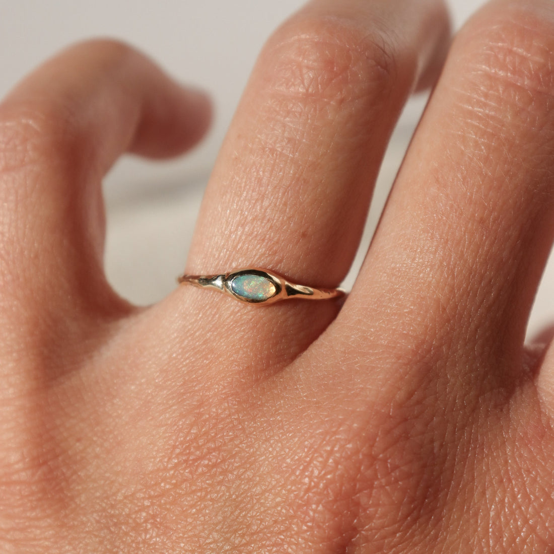 A tiny oval opal is  bezel set  in  14k gold on a narrow band.