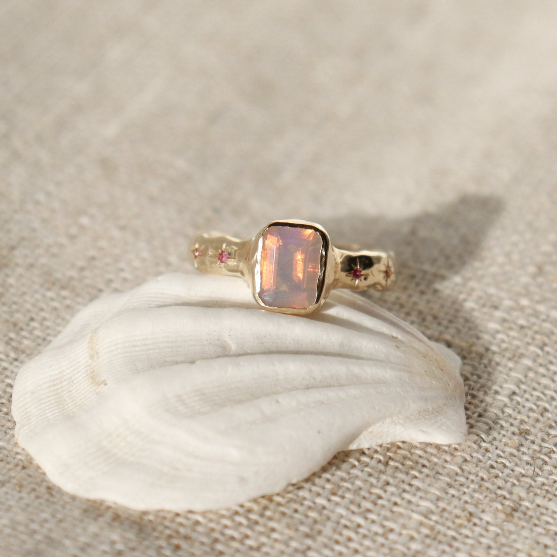 An emerald cut opal is bezel set in 14k gold with a wide band that features ombre sapphires star set a long each side of the band.