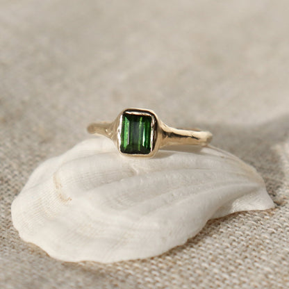 An emerald cut dark green tourmaline is bezel set in 14k gold on an organic band.