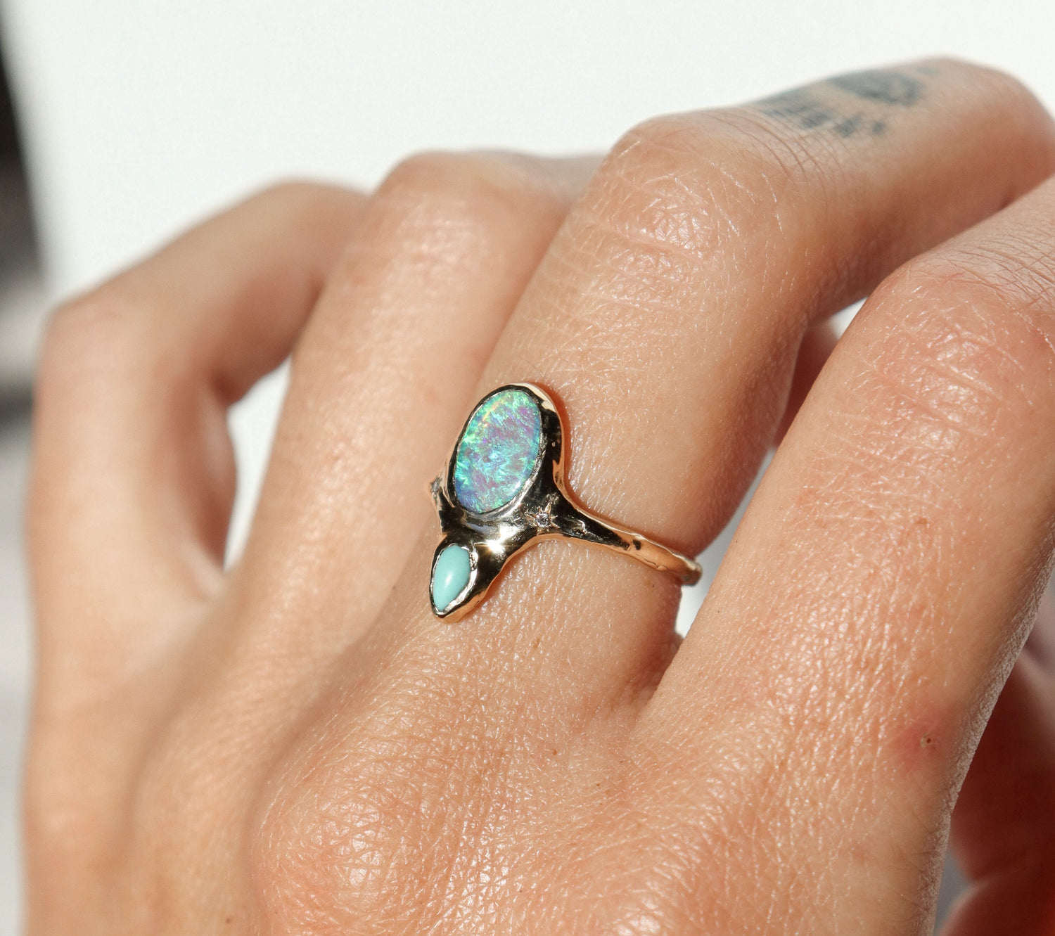 An oval opal is bezel set with a small pear shaped turquoise set underneath it,  this ring has two star set diamonds on each side  of  the center stone.