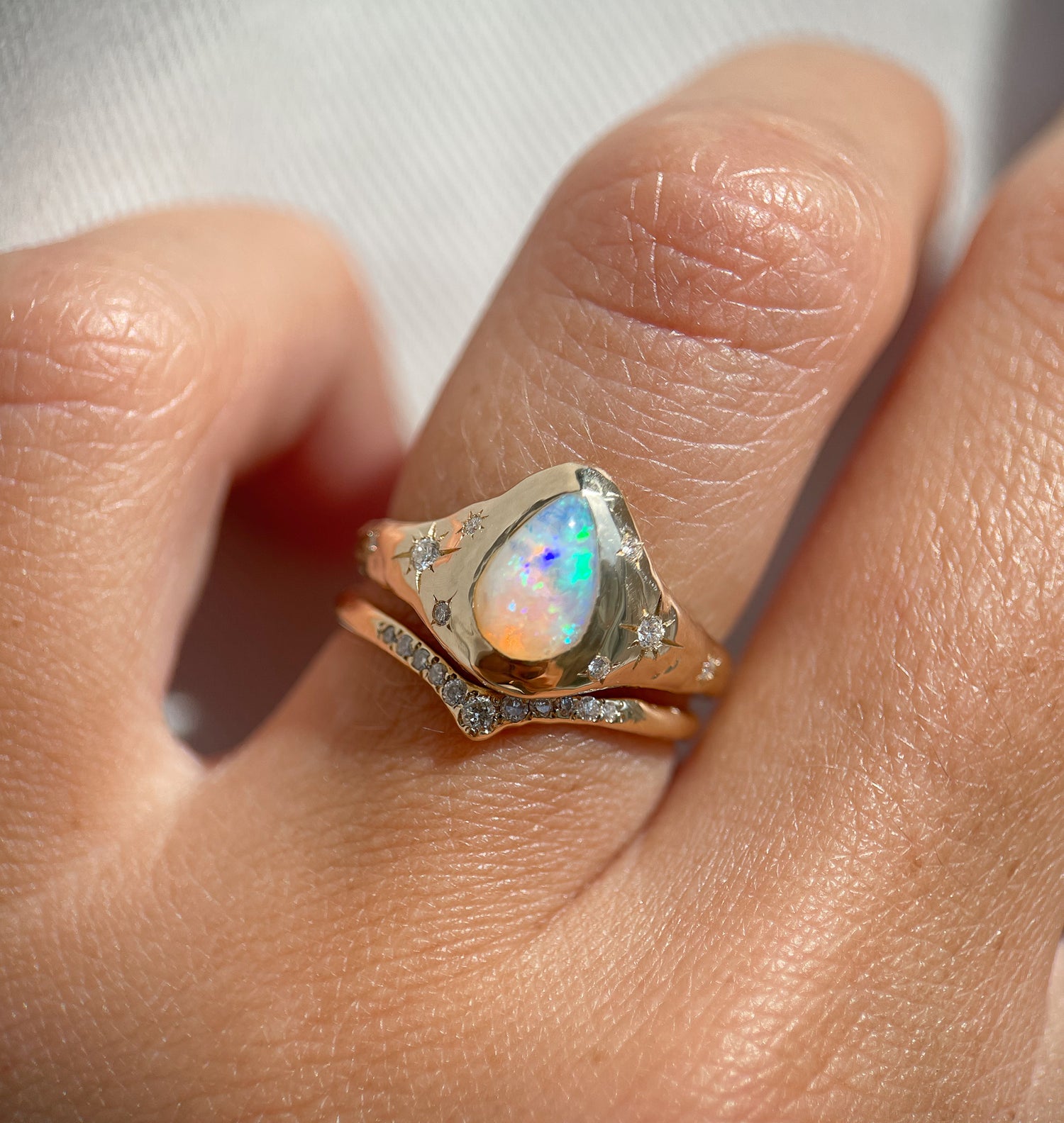 up close view of a gold opal ring that is signet style with star set diamond accents and paired with a pave diamond band
