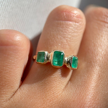 up close view of a trio emerald ring set in 14k gold worn on a ring finger