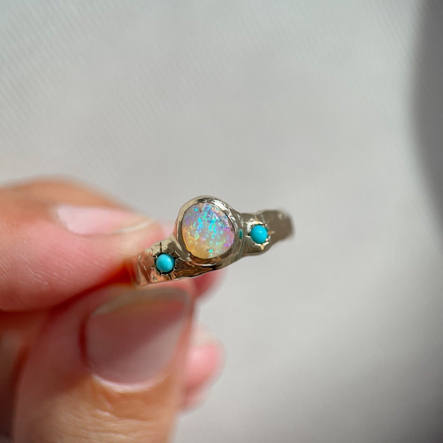 front view of a wide gold band with a center opal and turquoise star settings is worn on a ring finger