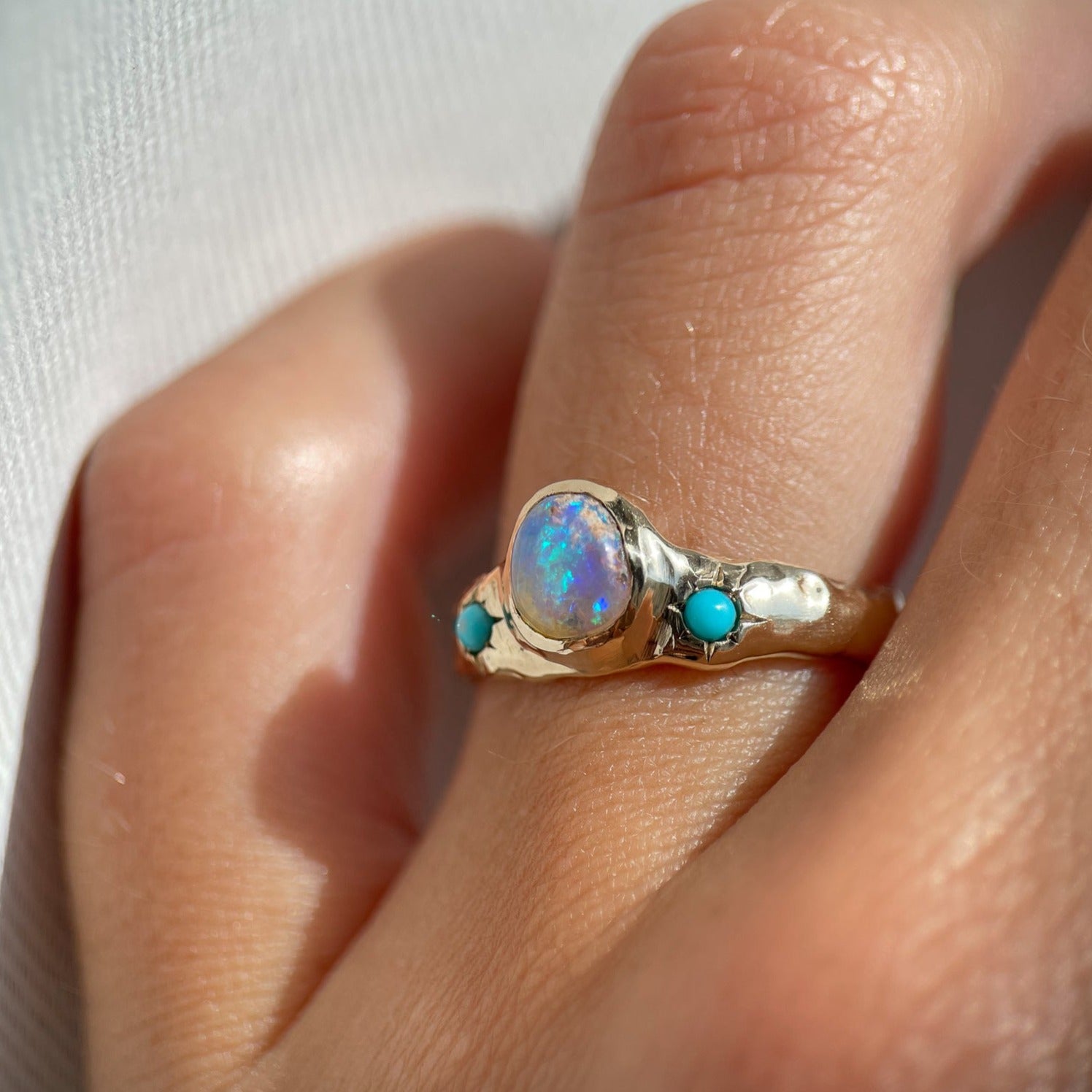 side view of a wide gold band with a center opal and turquoise star settings is worn on a ring finger
