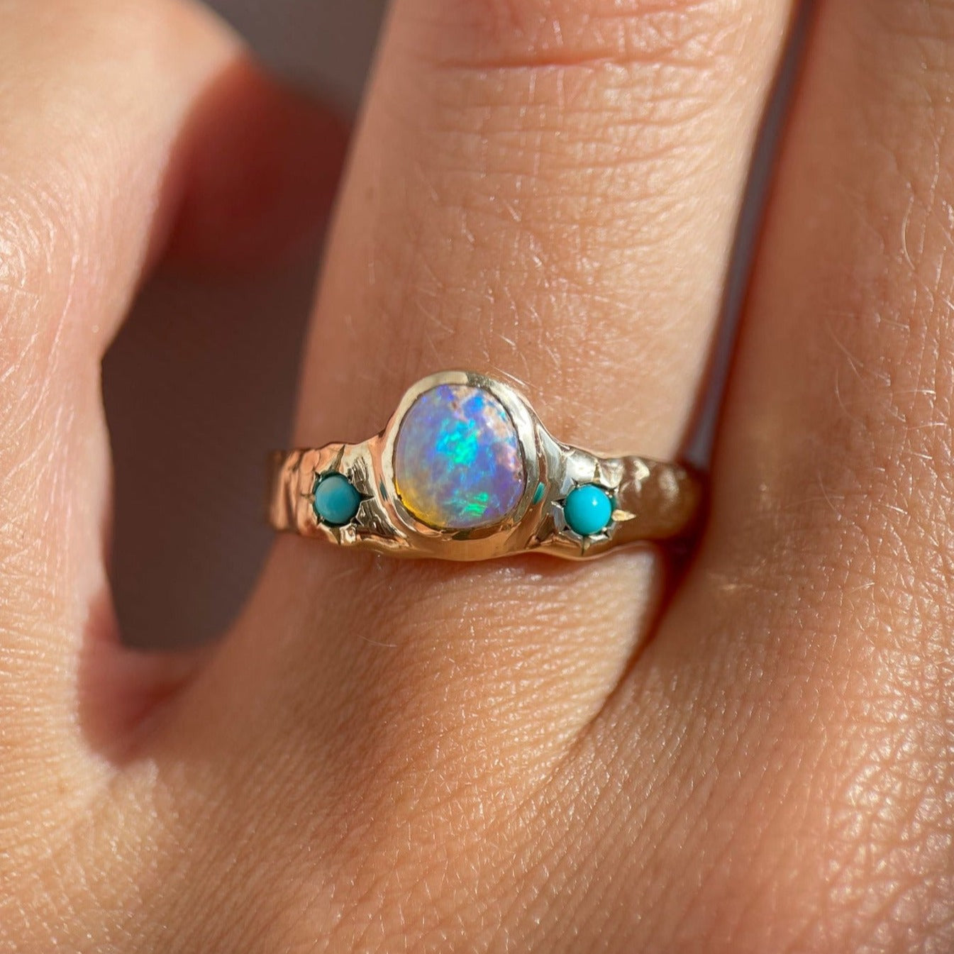 a wide gold band with a center opal and turquoise star settings is worn on a ring finger