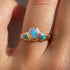 a wide gold band with a center opal and turquoise star settings is worn on a ring finger