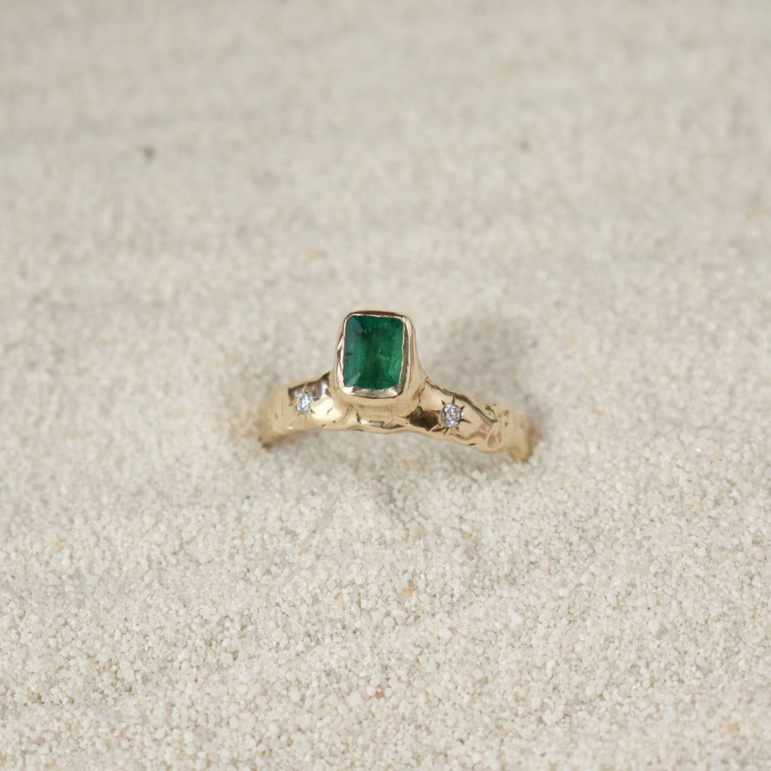 An emerald cut  emerald is bezel set in 14k gold  on a wide band with two star set diamonds on the side of the main stone.