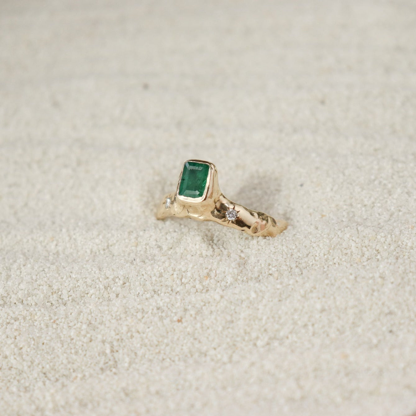 An emerald cut  emerald is bezel set in 14k gold  on a wide band with two star set diamonds on the side of the main stone.