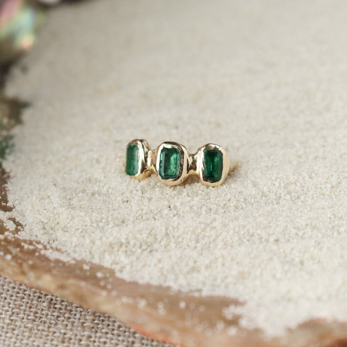 Three small emerald cut emeralds are embedded into a 14k gold ring giving it an organic look.