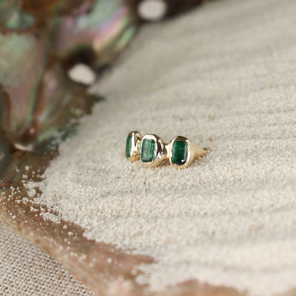 Side view of three small emerald cut emeralds embedded into a 14k gold ring giving it an organic look.