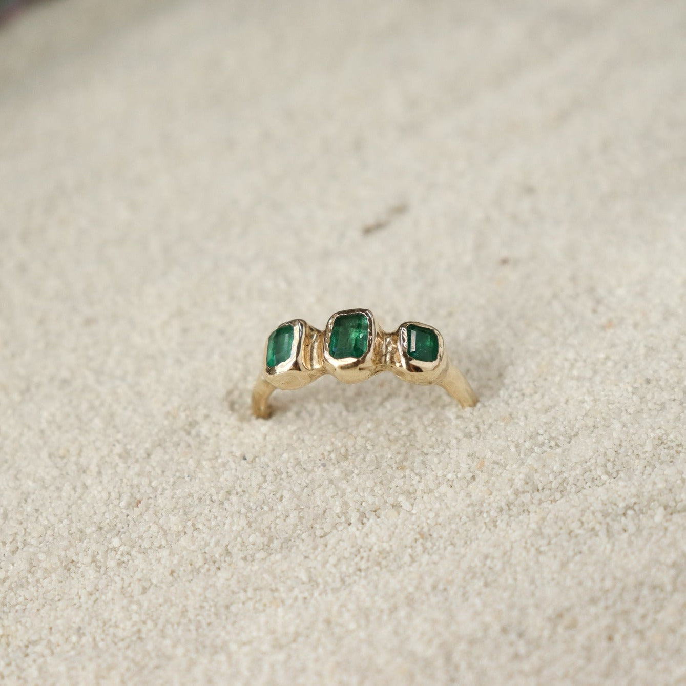 Three small emerald cut emeralds are embedded into a 14k gold ring giving it an organic  and handcrafted look.