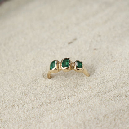 Three small emerald cut emeralds are embedded into a 14k gold ring giving it an organic  and handcrafted look.