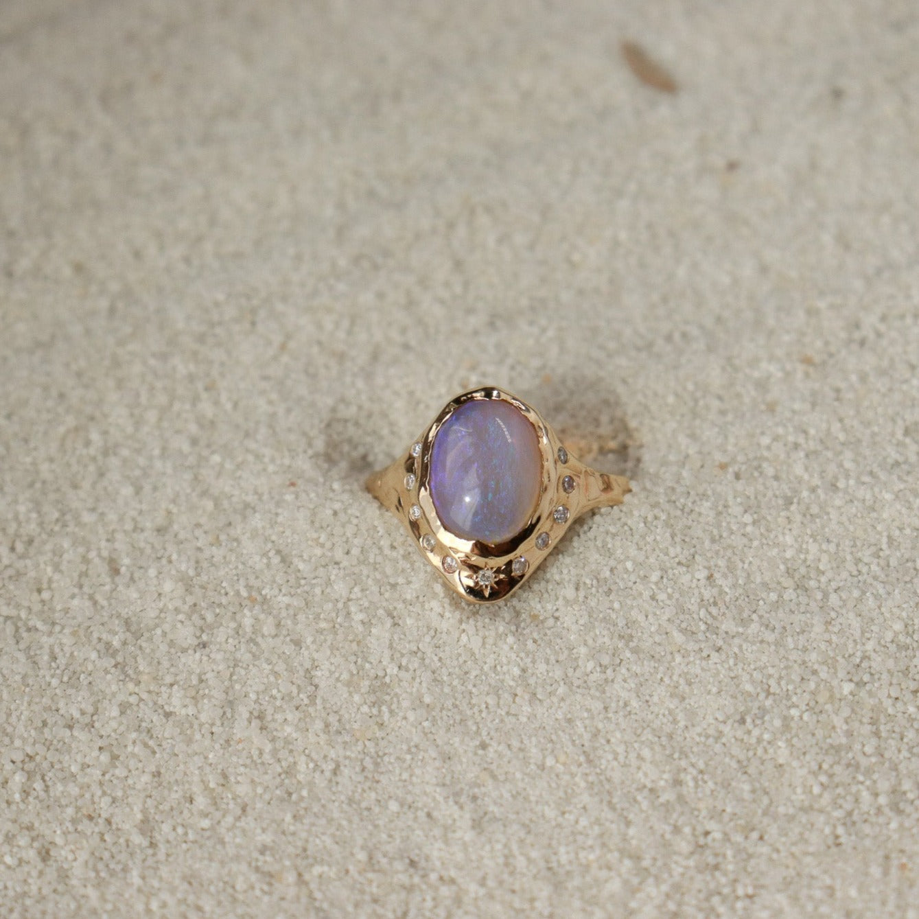 An oval opal is  bezel set in 14k gold with diamonds  set all around it,  there is a star set diamond at the base, and the band is organically crafted..