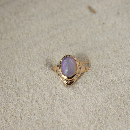 An oval opal is  bezel set in 14k gold with diamonds  set all around it,  there is a star set diamond at the base, and the band is organically crafted..