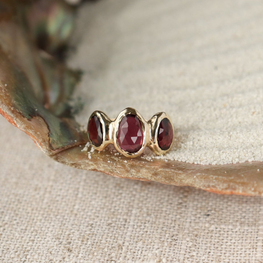 Three rose cut rhodolite garnets are bezel set  on an organically crafted 14k gold band.