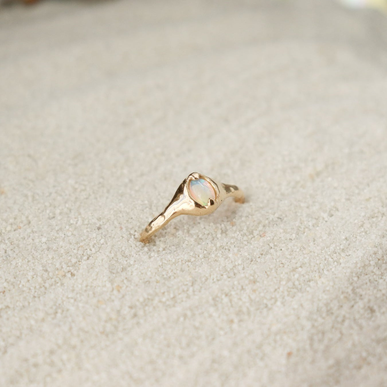A small oval opal ring is set with prongs on an organically crafted 14k gold band.