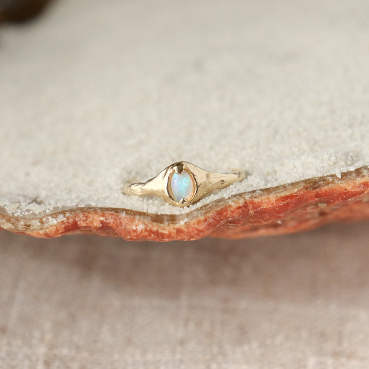A small oval opal ring is set with prongs on an organically crafted 14k gold band.