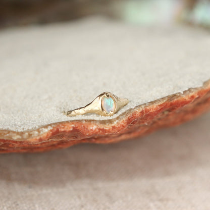 A small oval opal ring is set with prongs on an organically crafted 14k gold band.
