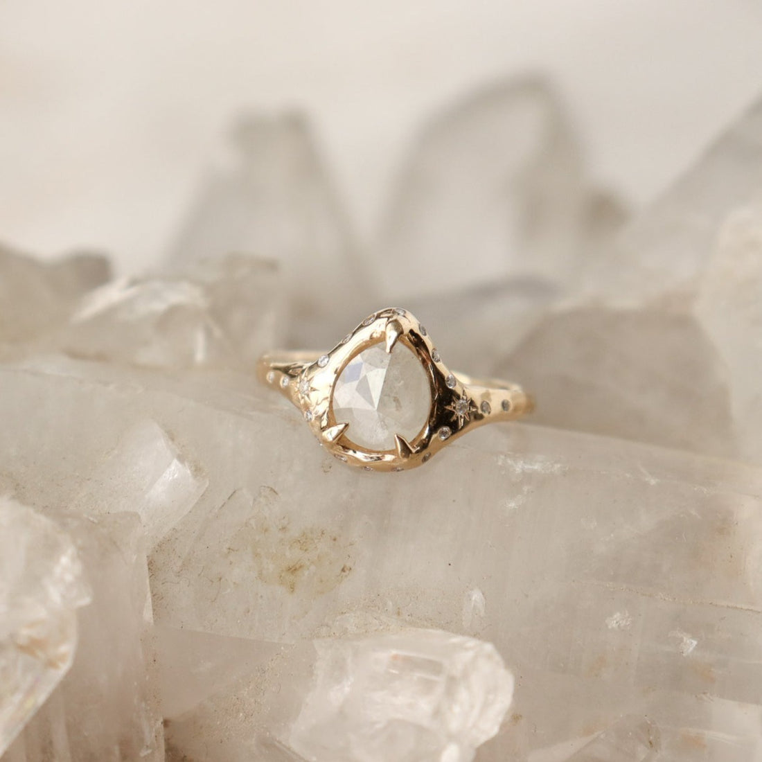 A pear shaped icy diamond is set with prongs and surrounded by diamonds on a 14k gold band.