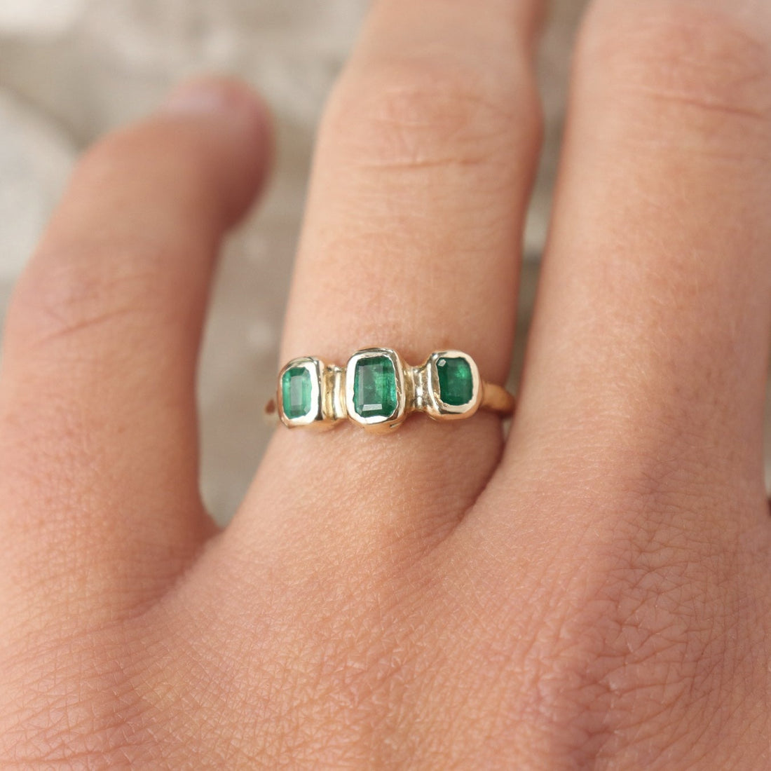 Three small emerald cut emeralds are embedded into a 14k gold ring giving it an organic  and handcrafted look.