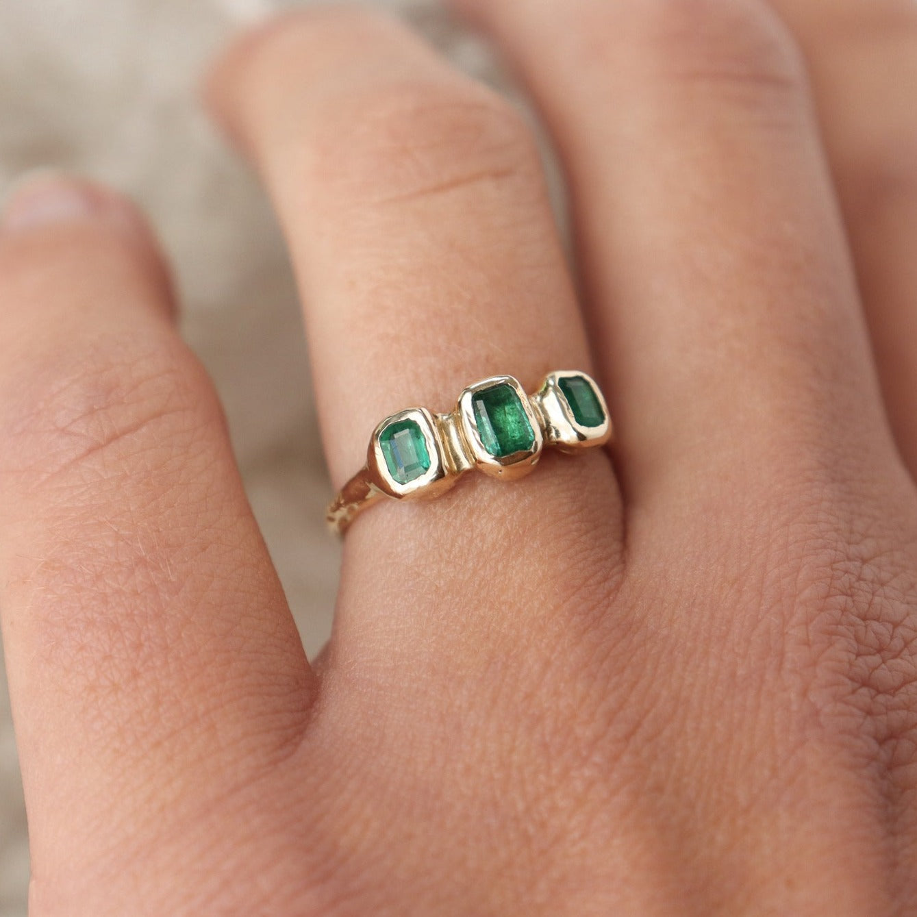 Worn on the ring finger, three small emerald cut emeralds are embedded into a 14k gold ring giving it an organic  and handcrafted look.