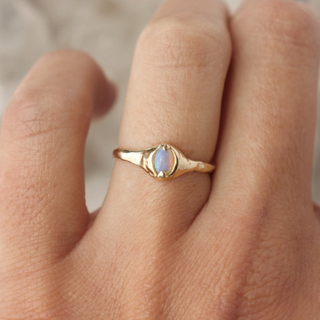 A small oval opal ring is set with prongs on an organically crafted 14k gold band.