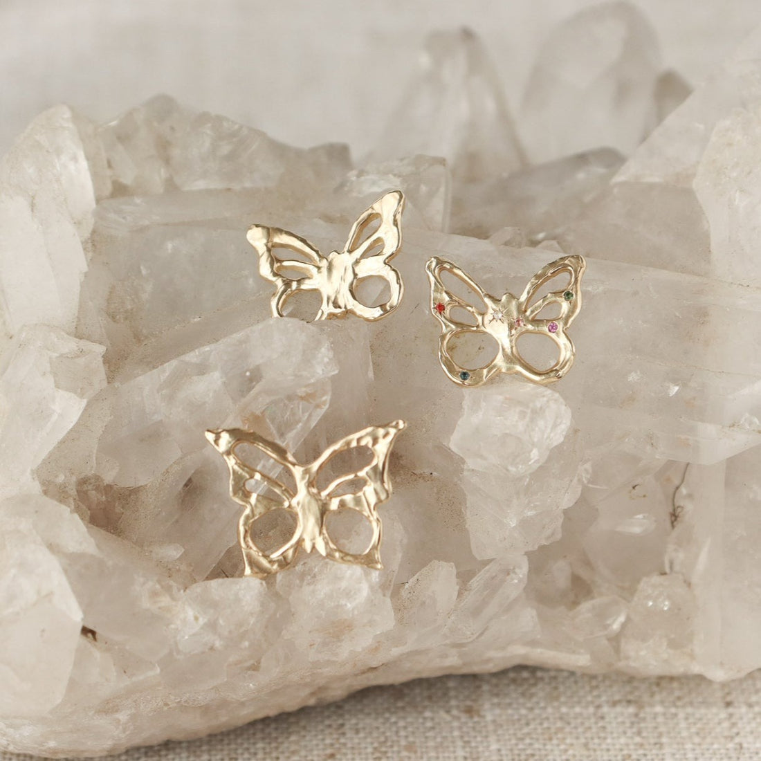An array of unique 14k gold  butterfly charms, all arranged atop  a crystal.