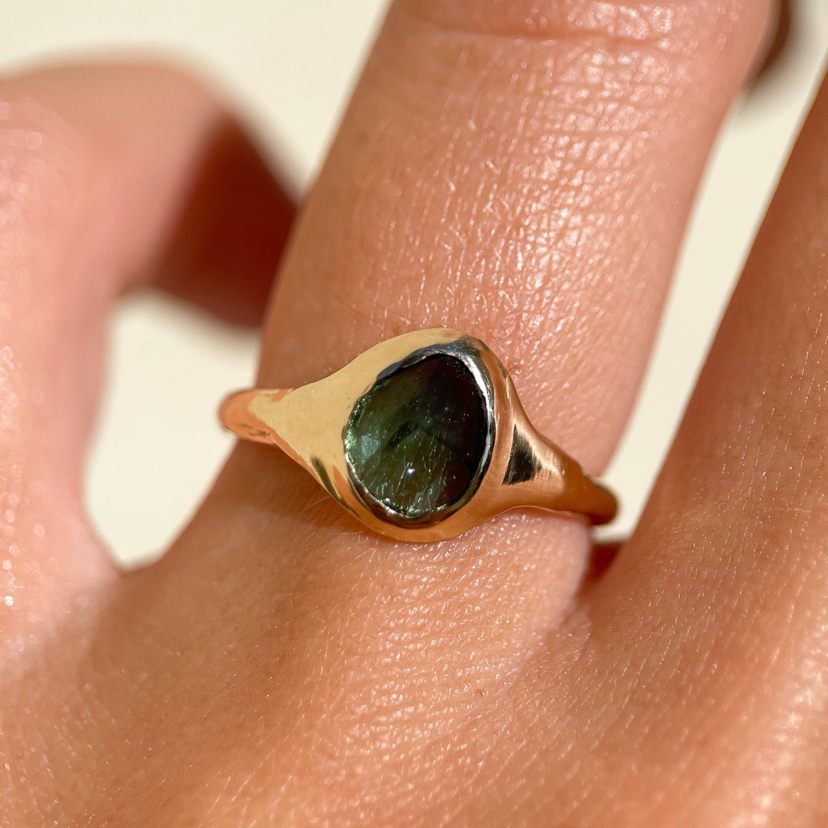 A rose cut blue green tourmaline is set in 14k  gold  into a signet style ring, worn on the ring finger.