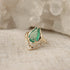 A pear shaped emerald is set with prongs and has a V-shape band under the stone with moonstones.