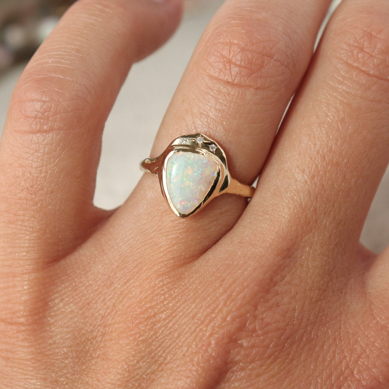 Front view of a white triangle opal is bezel set in 14k gold with three star set diamonds.