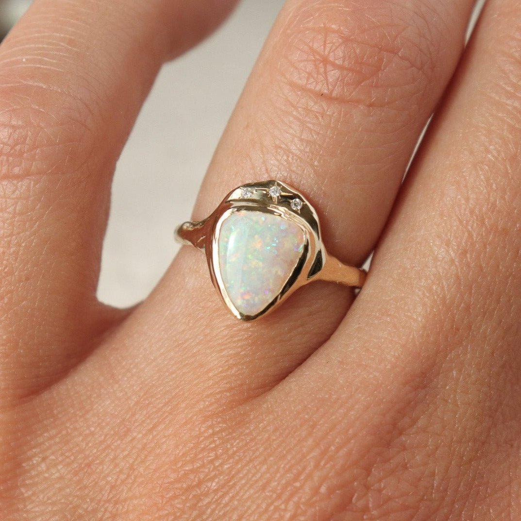 Front view of a white triangle opal is bezel set in 14k gold with three star set diamonds.