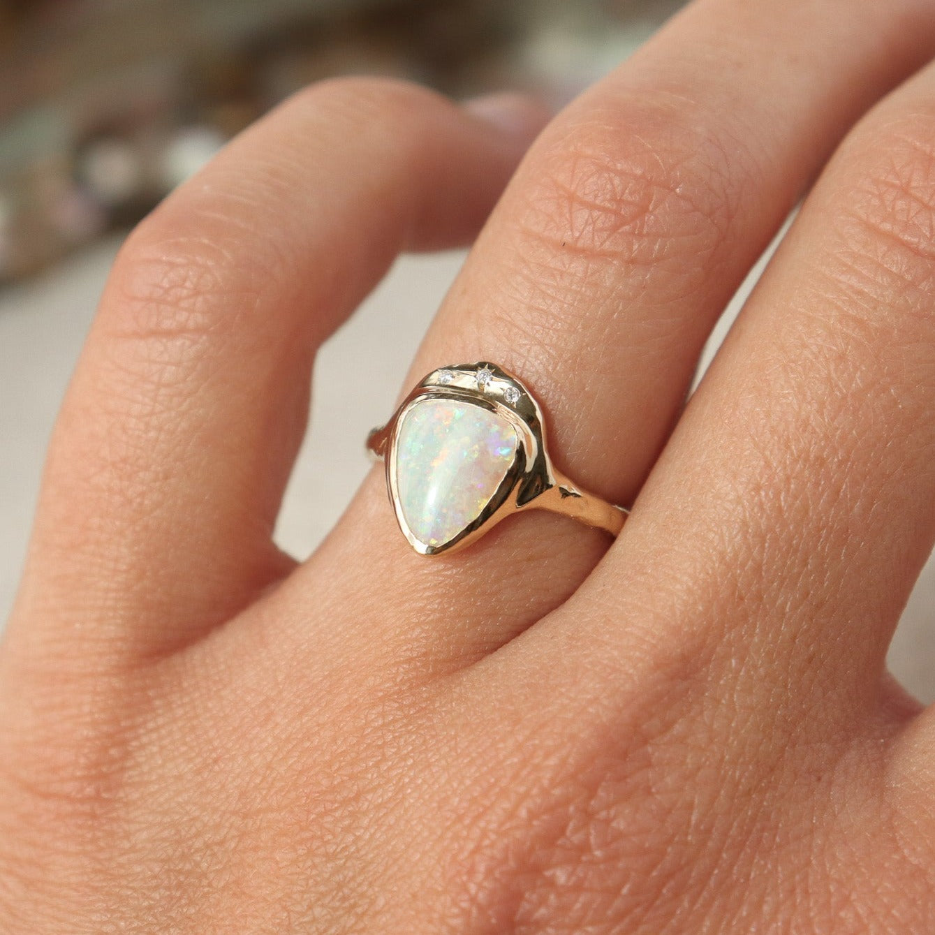 White triangle opal is bezel set in 14k gold with three star set diamonds, worn on the ring finger.