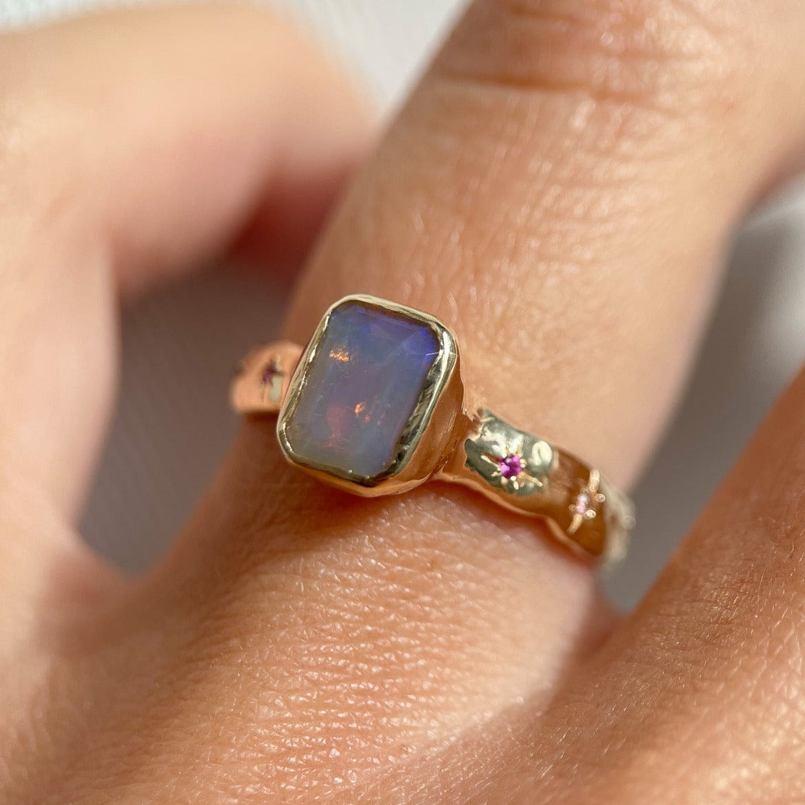 An emerald cut opal is bezel  set  in 14k  gold  with a wide  band that  features  ombre sapphires  star  set a long  each side of the band.