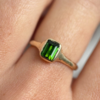 An emerald cut dark green tourmaline is bezel set in 14k gold on an organic band.