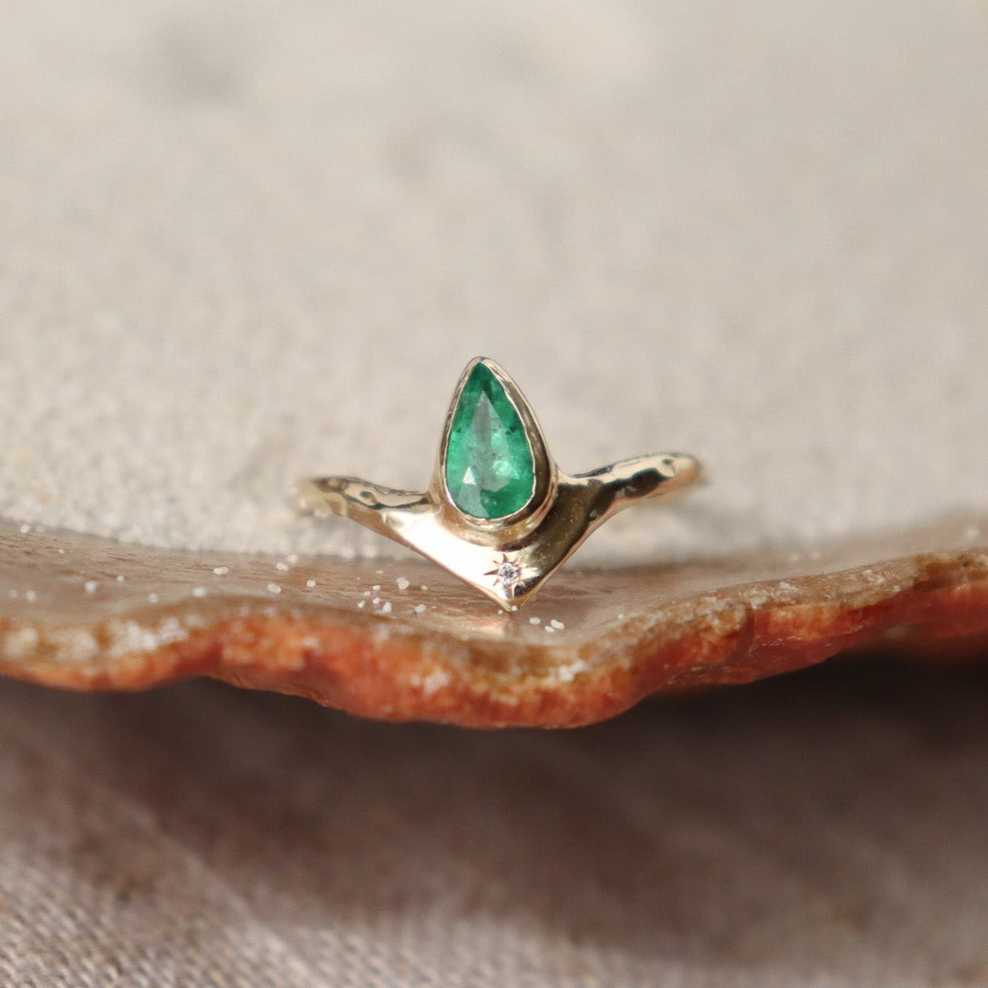 Pear-shaped emerald bezel-set with a brilliant diamond star at its base, creating a striking and celestial-inspired jewelry piece.