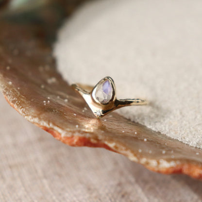 Pear-shaped moonstone, bezel-set with a dazzling diamond star positioned at the base for a celestial-inspired and enchanting ring design.