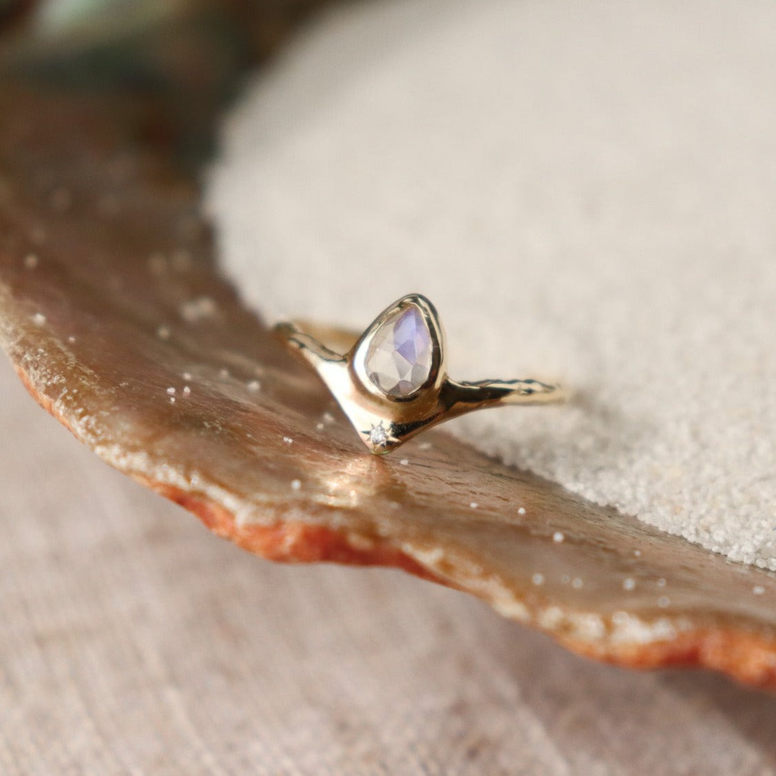 Pear-shaped moonstone, bezel-set with a dazzling diamond star positioned at the base for a celestial-inspired and enchanting ring design.