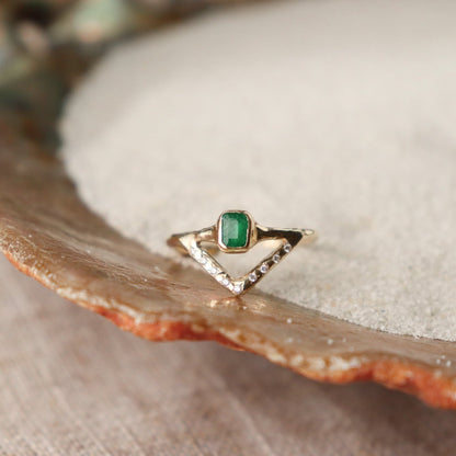 Stunning emerald ring with a bezel-set, rich green gemstone elegantly perched on a delicate, narrow band. Beneath it, a gracefully designed V-band features organically set diamonds, adding a touch of nature-inspired luxury to your jewelry collection.